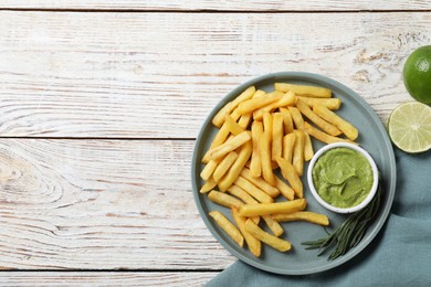 Photo of Plate with delicious french fries, avocado dip, lime and rosemary served on white wooden table, top view. Space for text