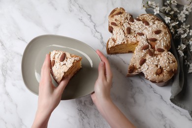 Photo of Woman with piece of delicious Italian Easter dove cake (traditional Colomba di Pasqua) at white marble table, above view