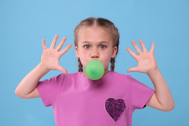 Surprised girl in sunglasses blowing bubble gum on light blue background