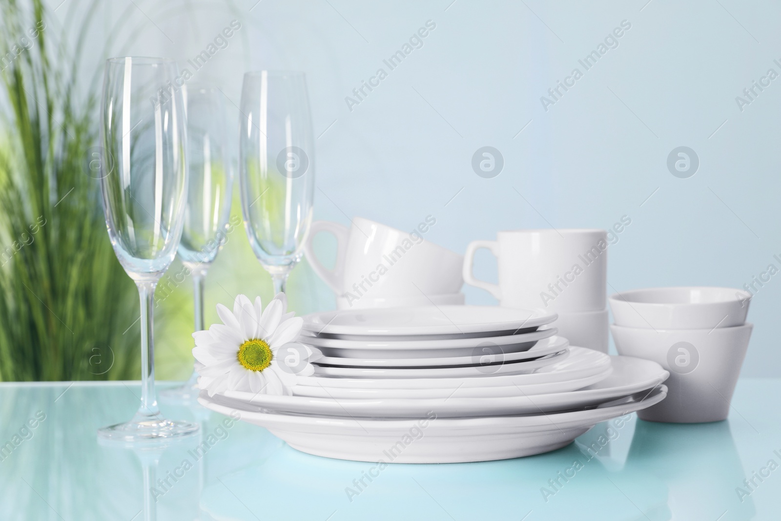 Photo of Set of clean dishware and flower on light blue table