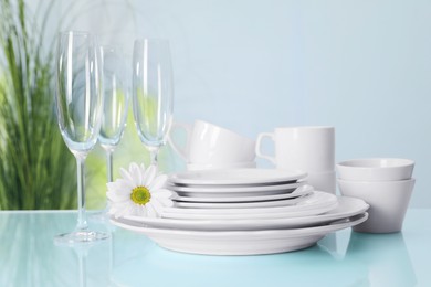 Set of clean dishware and flower on light blue table