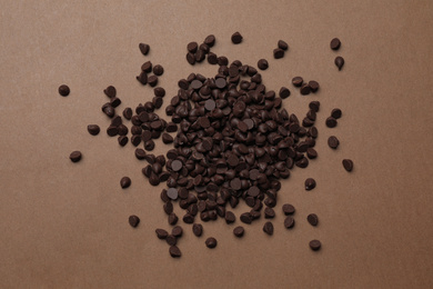 Photo of Pile of delicious chocolate chips on brown background, top view