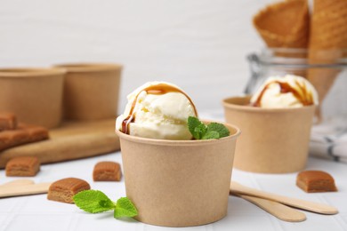 Photo of Scoopsice cream with caramel sauce, mint leaves and candies on white tiled table, closeup