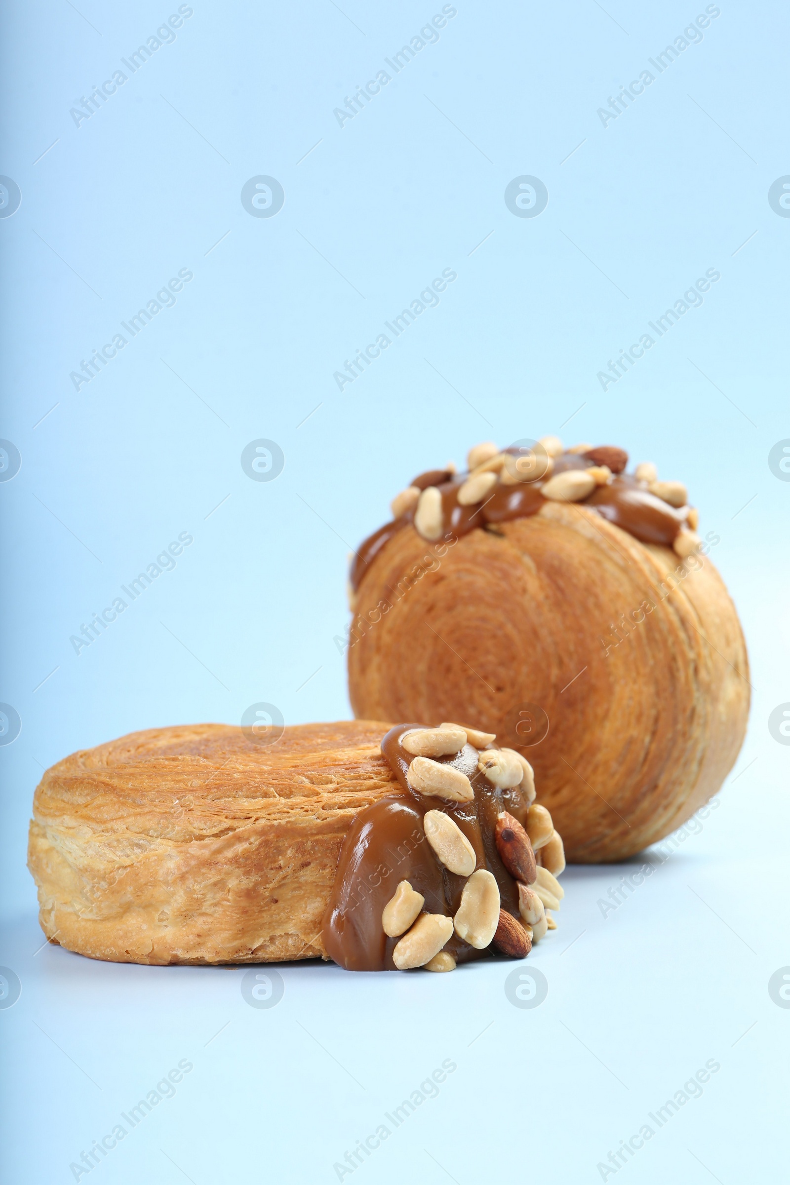 Photo of Supreme croissants with chocolate paste and nuts on light blue background. Tasty puff pastry