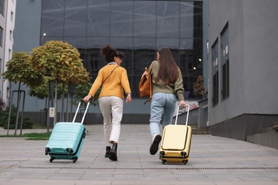 Photo of Being late. Women with suitcases walking towards building outdoors, back view