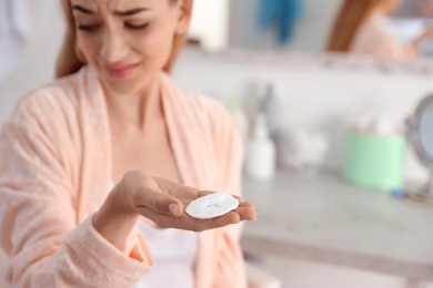 Young woman holding cotton pad with fallen eyelashes indoors