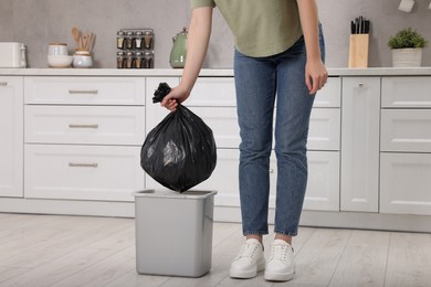 Photo of Woman taking garbage bag out of trash bin in kitchen, closeup