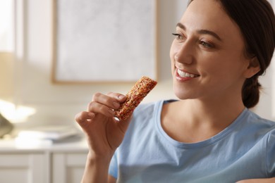 Photo of Woman holding tasty granola bar at home