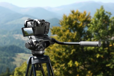 Photo of Tripod with modern camera in mountains on sunny day