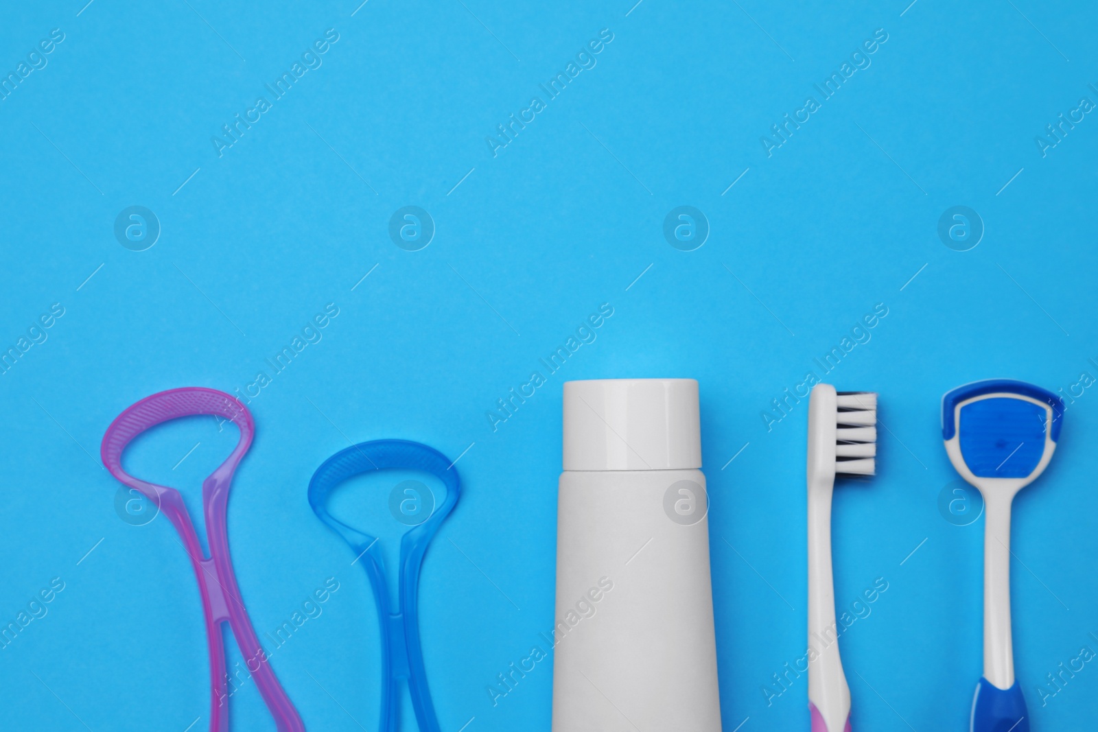 Photo of Tongue cleaners, toothbrush and paste on blue background, flat lay. Space for text