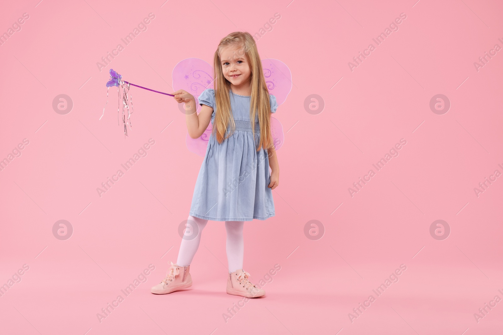 Photo of Cute little girl in fairy costume with violet wings and magic wand on pink background