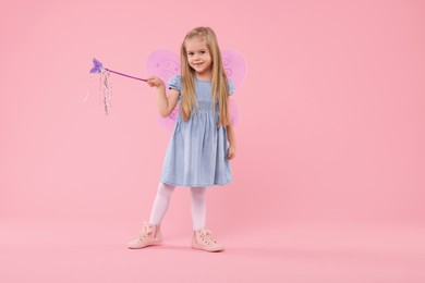 Photo of Cute little girl in fairy costume with violet wings and magic wand on pink background