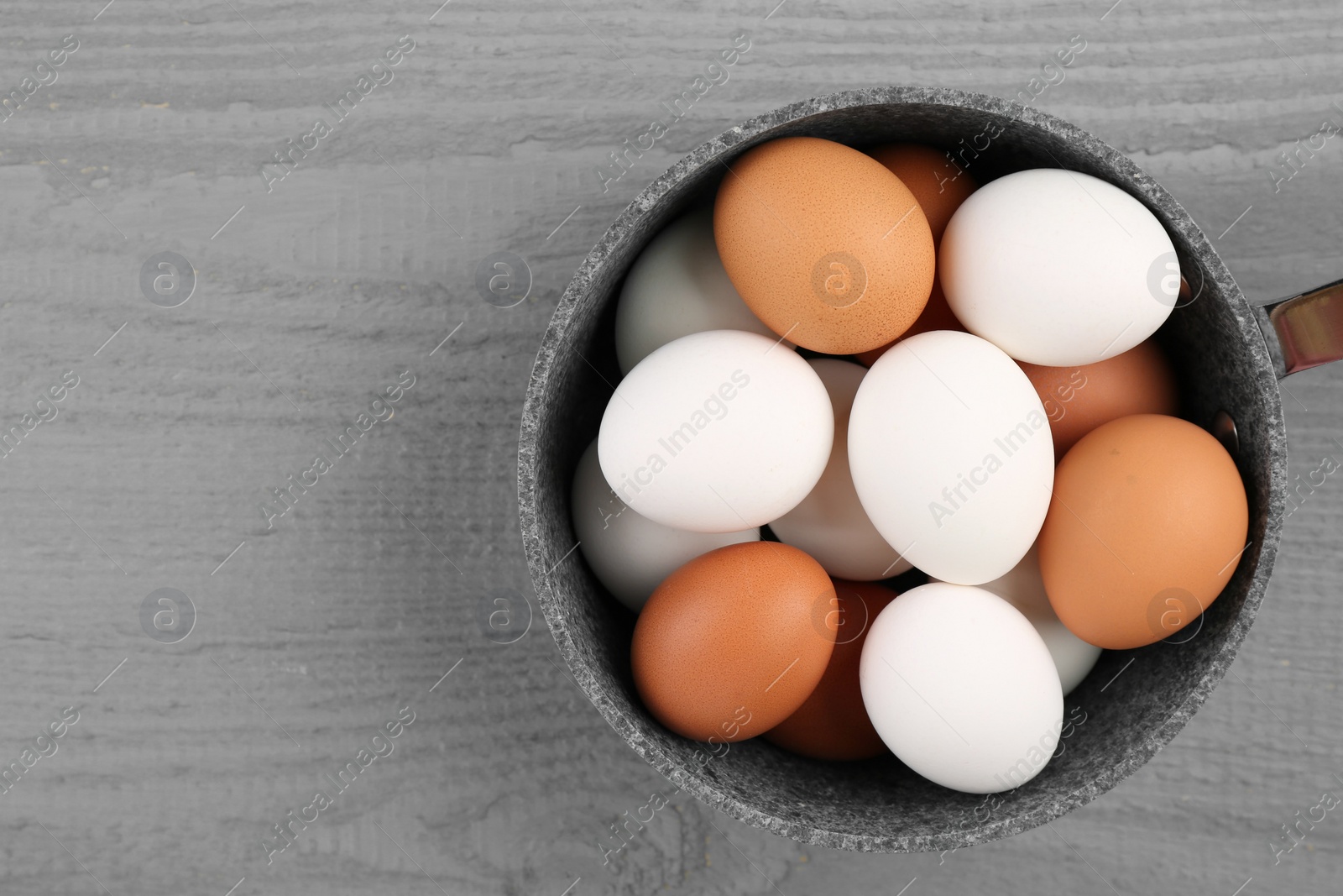Photo of Unpeeled boiled eggs in saucepan on grey wooden table, top view. Space for text