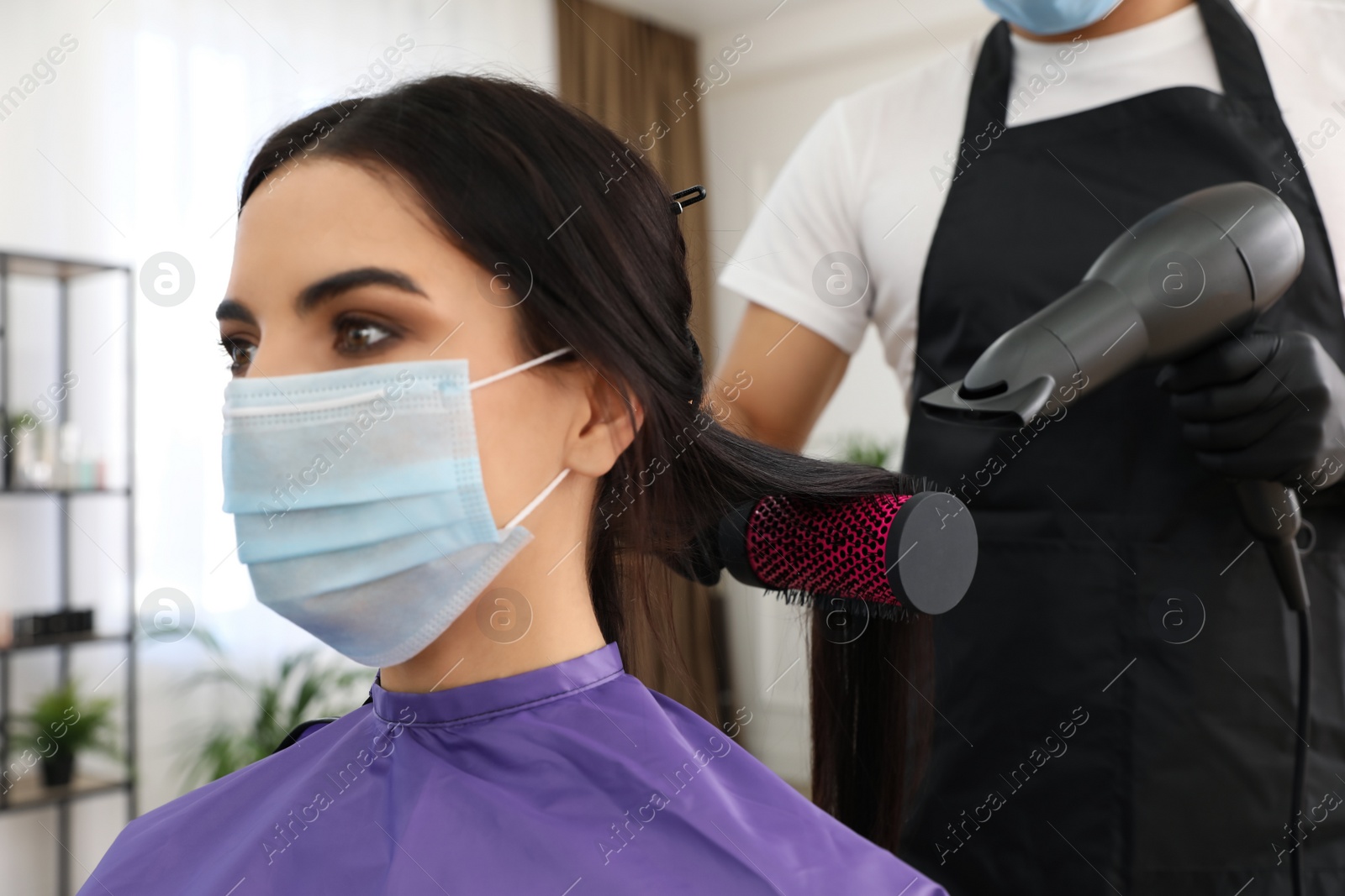 Photo of Professional stylist working with client in salon, closeup. Hairdressing services during Coronavirus quarantine