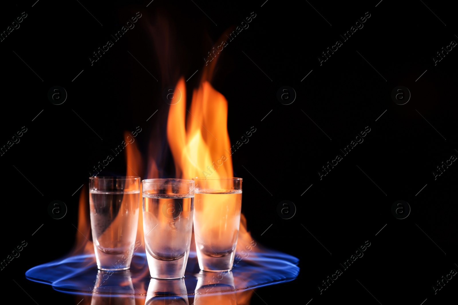 Photo of Vodka in shot glasses and flame on black background, space for text