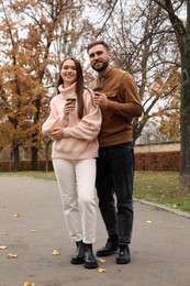 Photo of Happy couple wearing stylish clothes with cups of coffee in autumn park