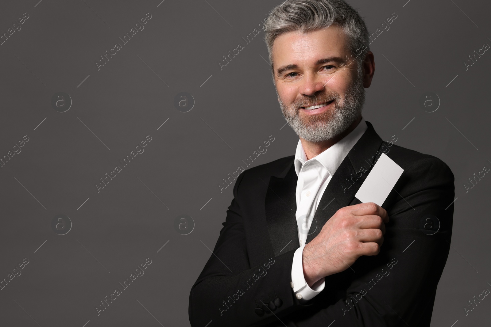Photo of Smiling man holding blank business card on grey background. Space for text
