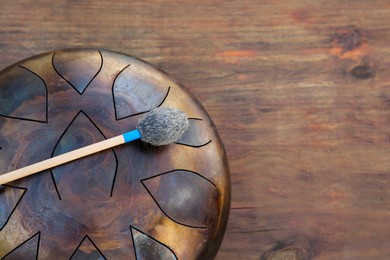 Photo of Steel tongue drum with soft mallet on wooden table, top view and space for text. Percussion musical instrument