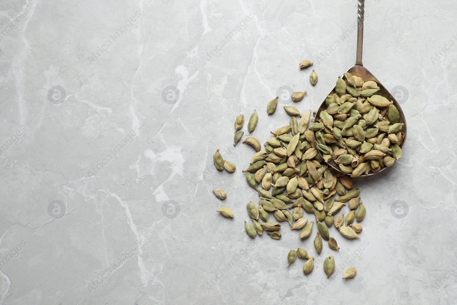 Photo of Spoon with dry cardamom pods on grey marble table, top view. Space for text