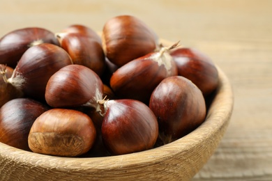 Fresh sweet edible chestnuts in wooden bowl on table, closeup