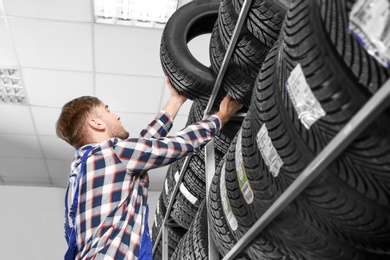 Young male mechanic with car tires in automobile service center