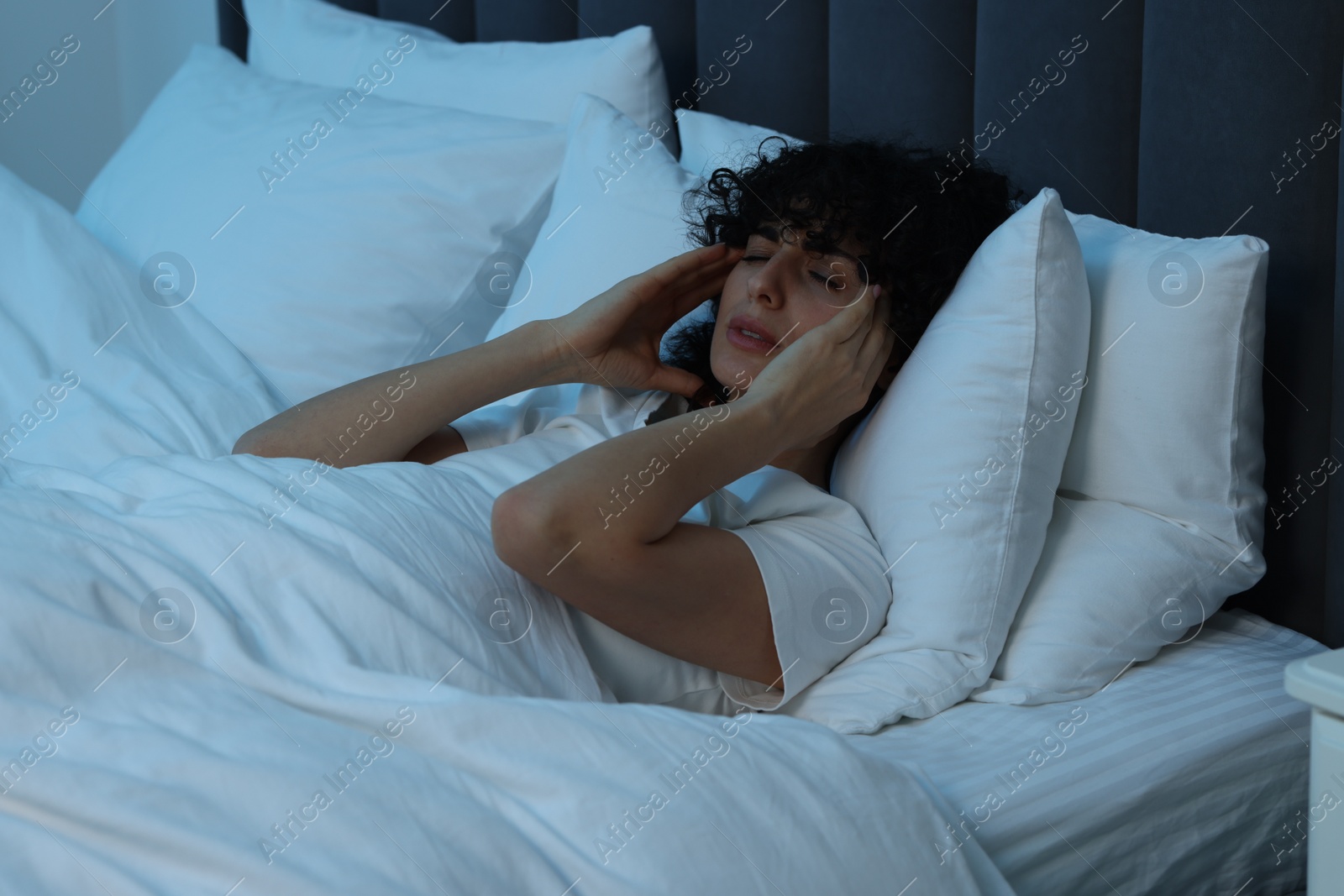 Photo of Young woman suffering from headache in bed at night