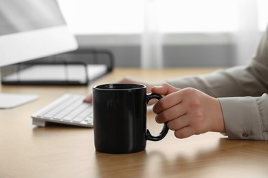 Photo of Woman with black ceramic mug at workplace, closeup