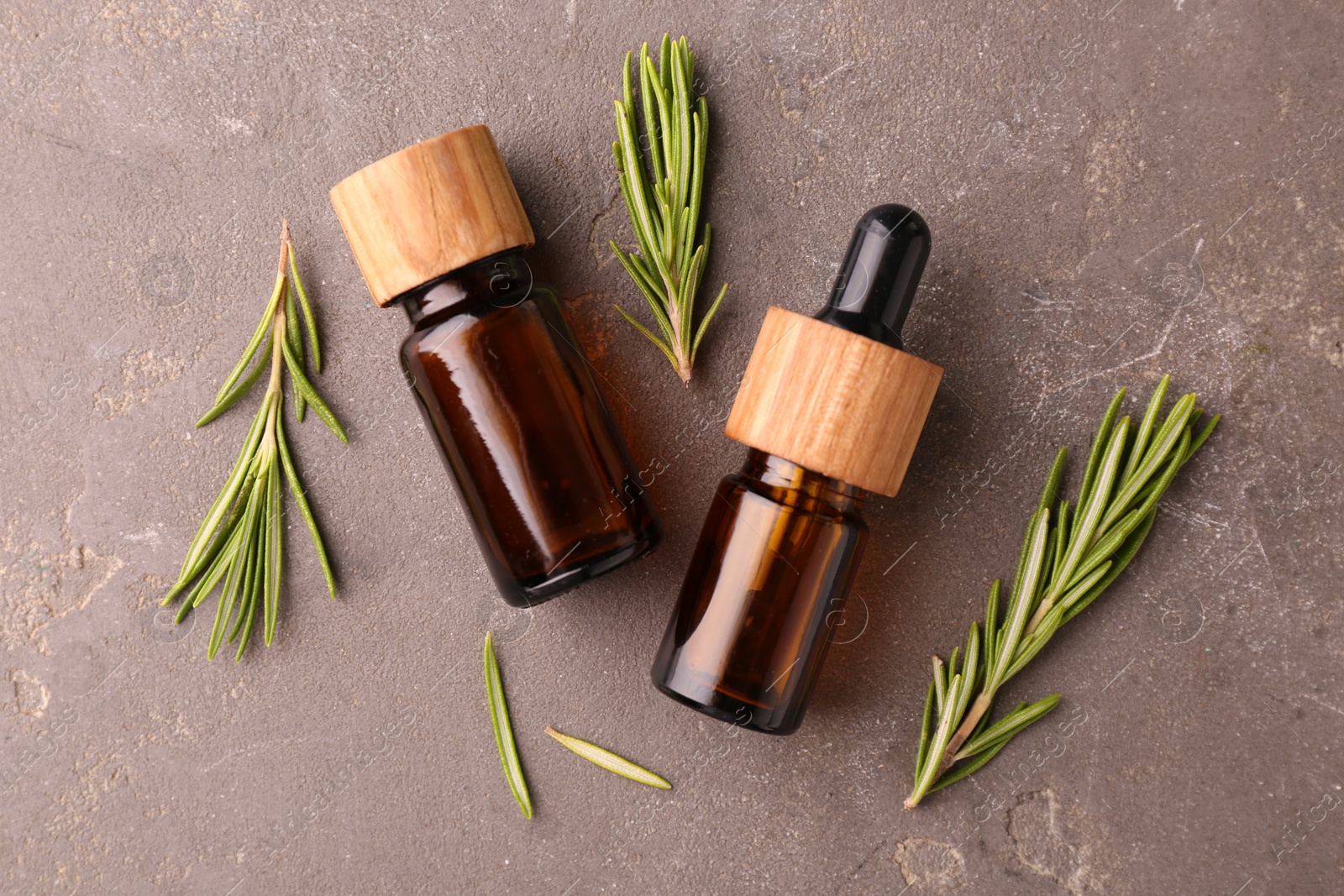 Photo of Essential oil in bottles and rosemary on grey table, flat lay