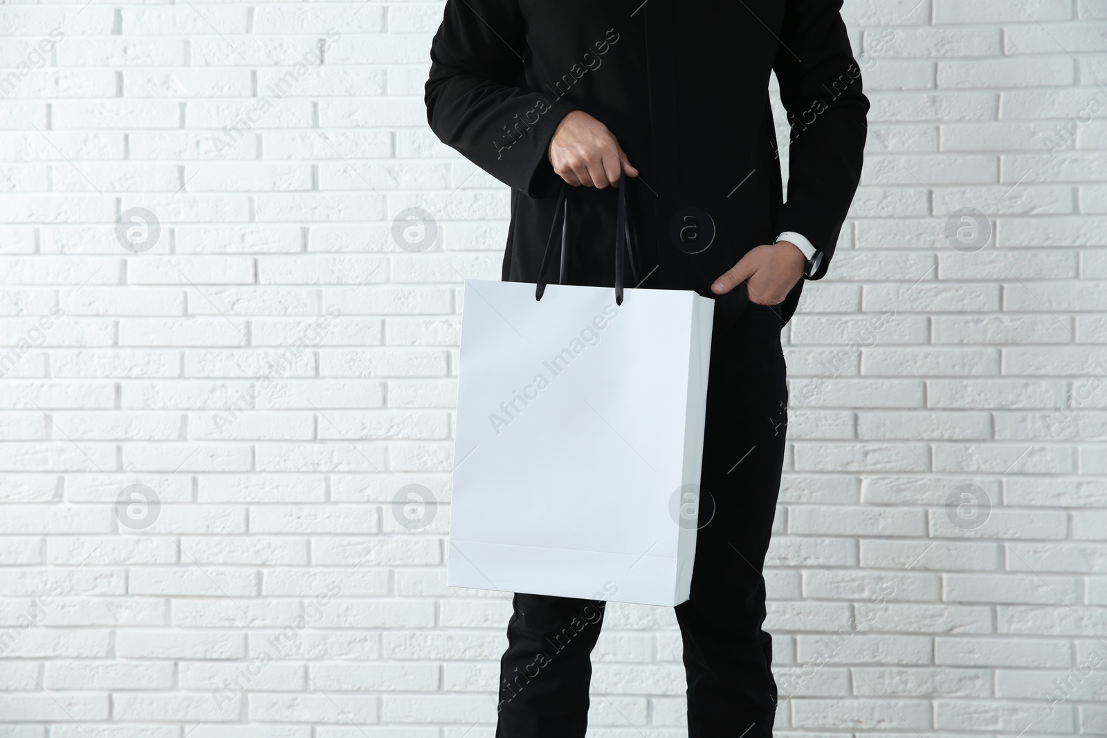 Photo of Young man holding paper bag against brick wall, closeup.  Mockup for design