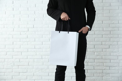 Young man holding paper bag against brick wall, closeup.  Mockup for design