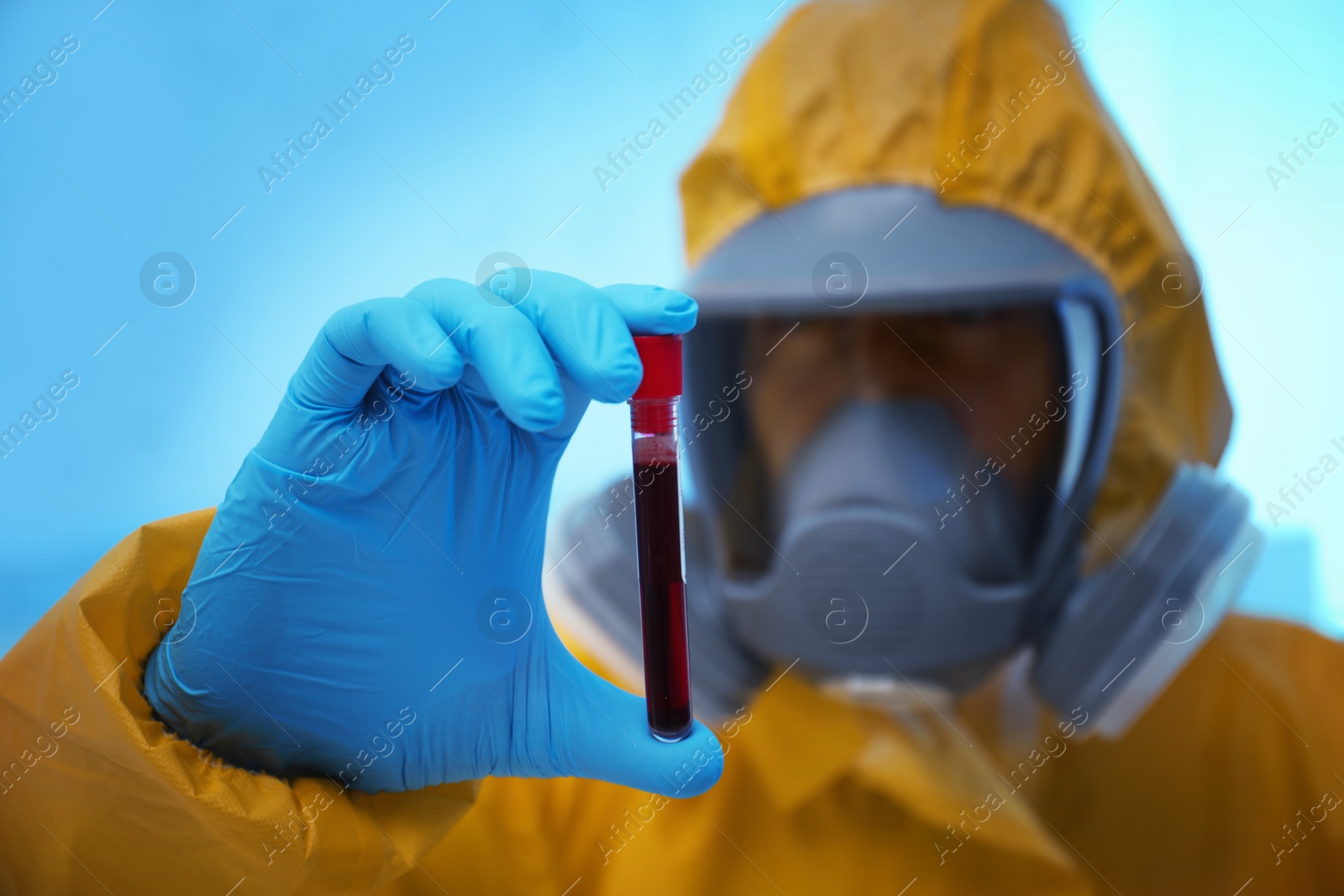 Photo of Scientist in chemical protective suit holding blood sample at laboratory, focus on test tube. Virus research