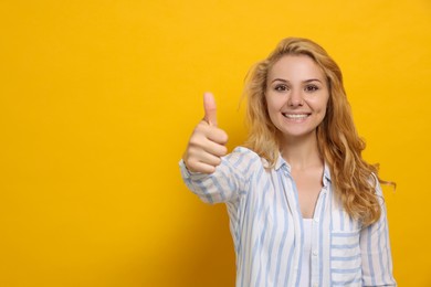 Photo of Happy young woman showing thumb up gesture on yellow background. Space for text