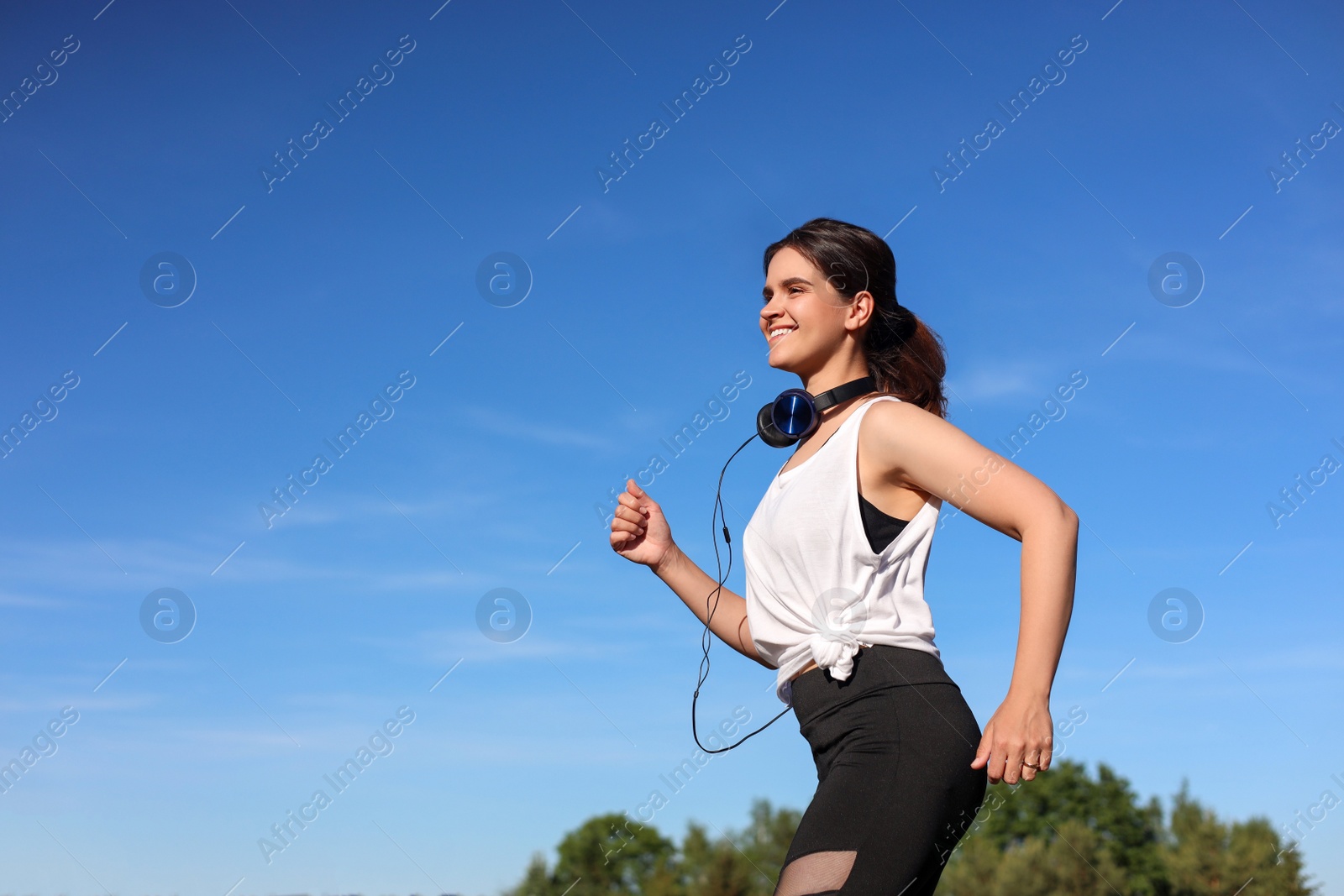 Photo of Young woman with headphones running outdoors in morning. Space for text