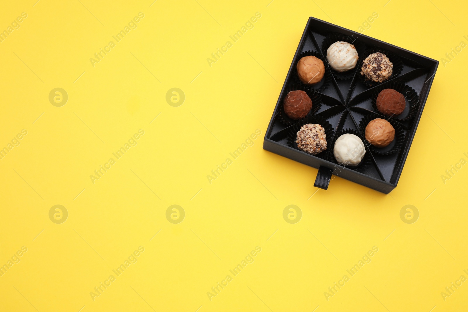 Photo of Box of tasty chocolate candies on yellow background, top view. Space for text