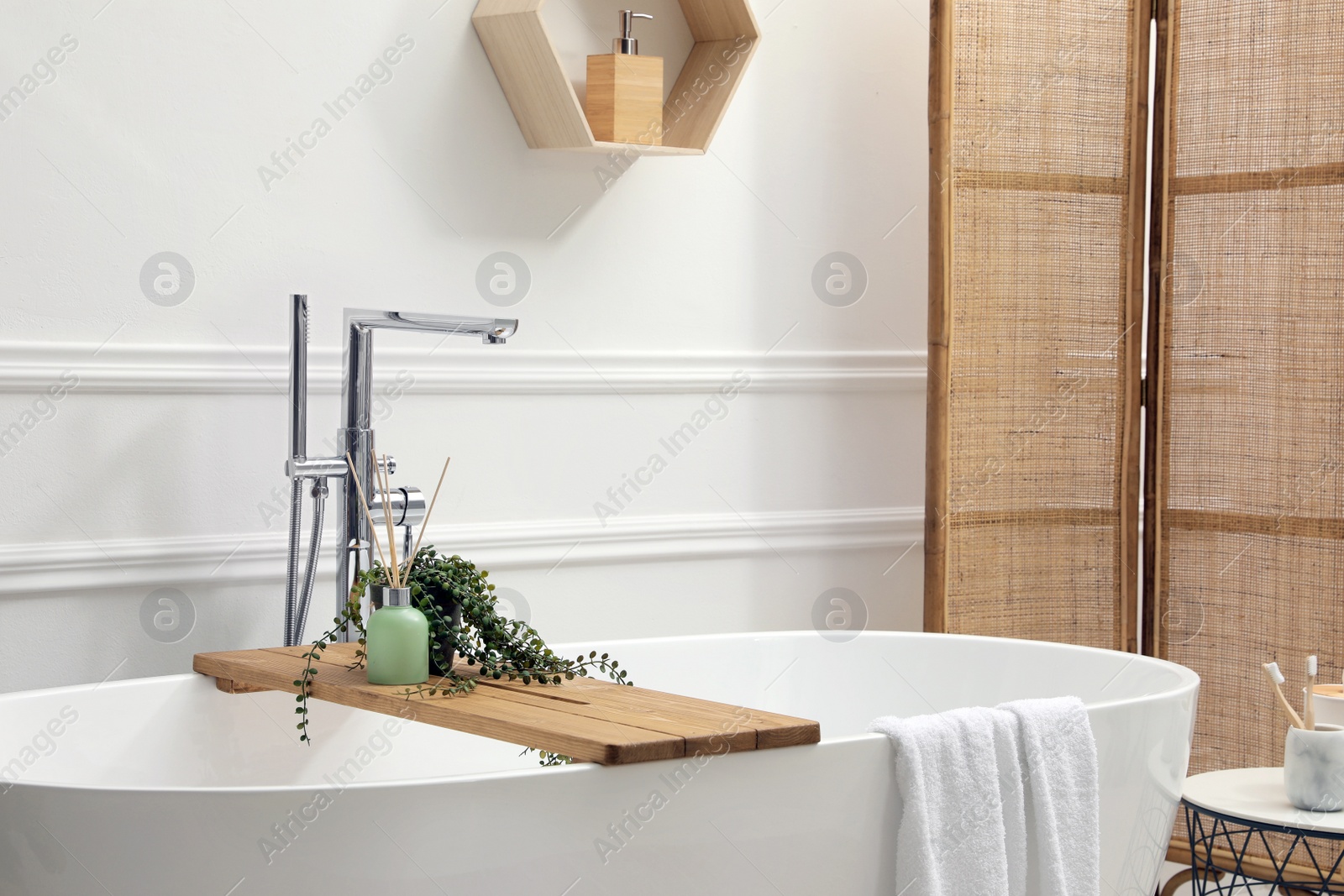 Photo of Modern ceramic bathtub and green plant near white wall in room