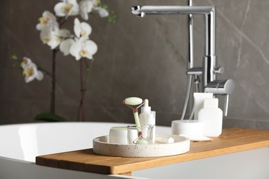 Bath tray with natural face roller and cosmetic products on tub