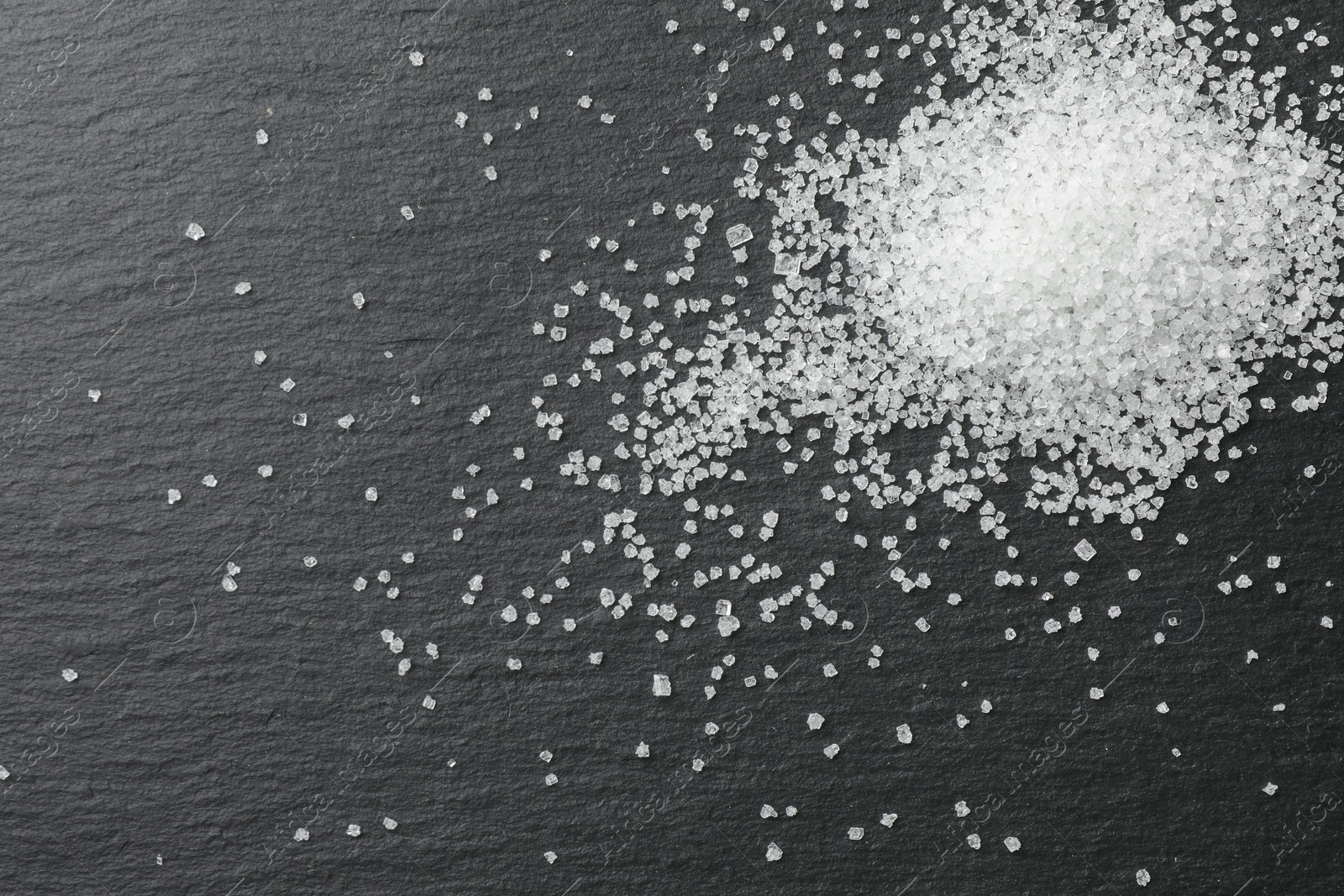 Photo of Heap of granulated sugar on black table, top view. Space for text