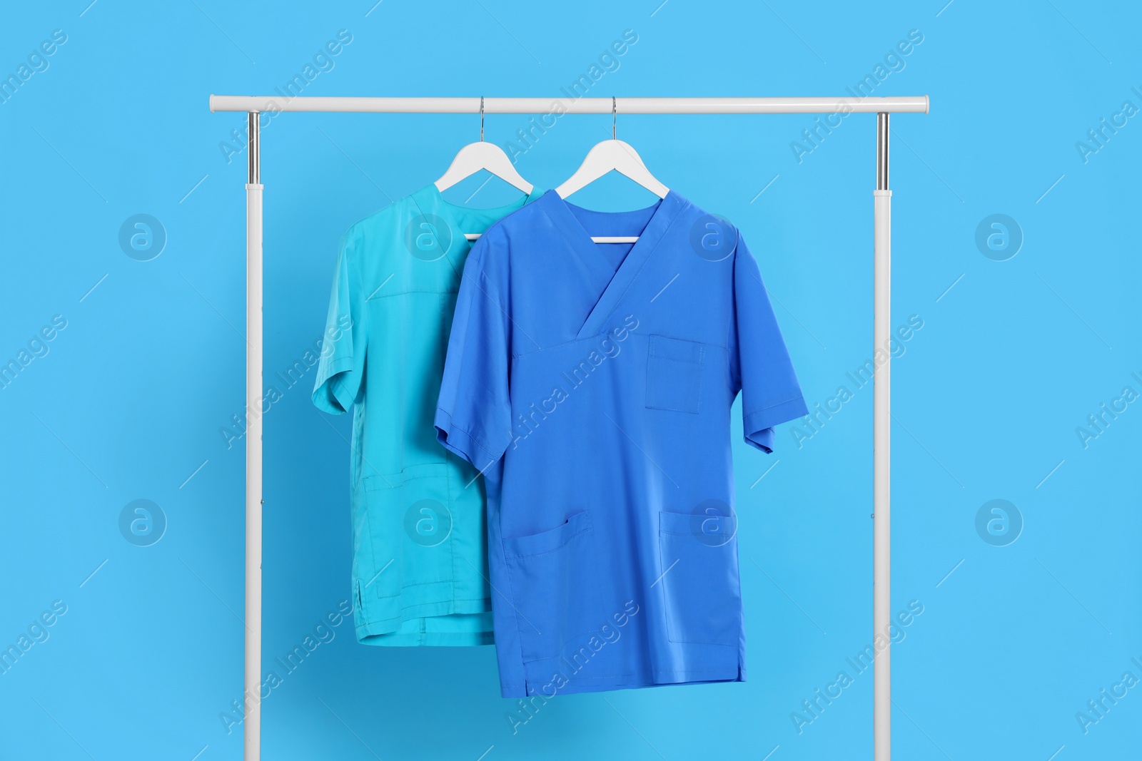 Photo of Medical uniforms on rack against light blue background