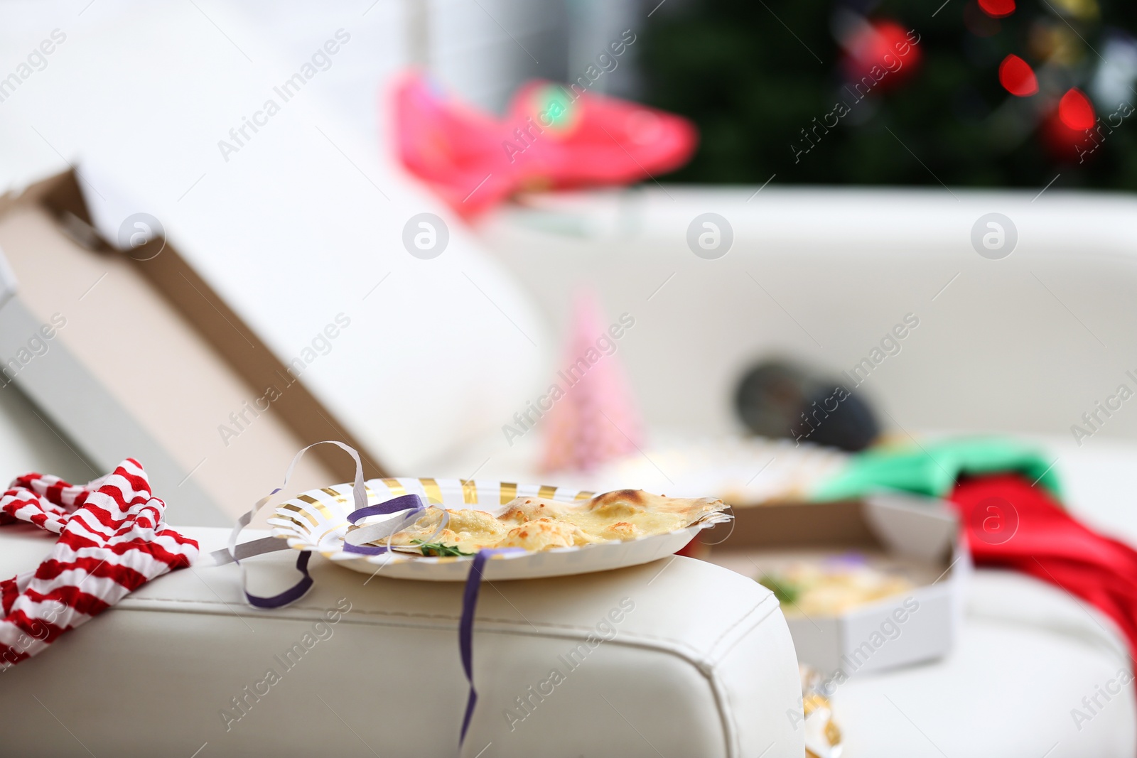 Photo of Plate with piece of pizza and streamer on sofa indoors, space for text. Chaos after party