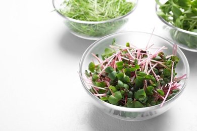 Photo of Glass bowl with fresh microgreen on white table, closeup. Space for text
