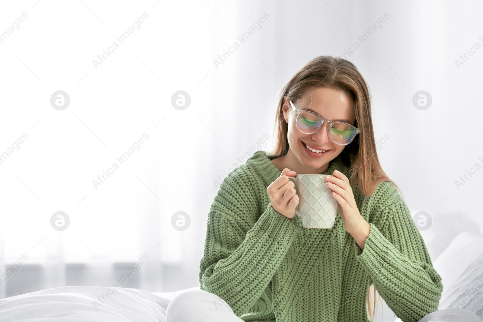 Photo of Young woman in warm sweater with hot drink on bed at home. Space for text