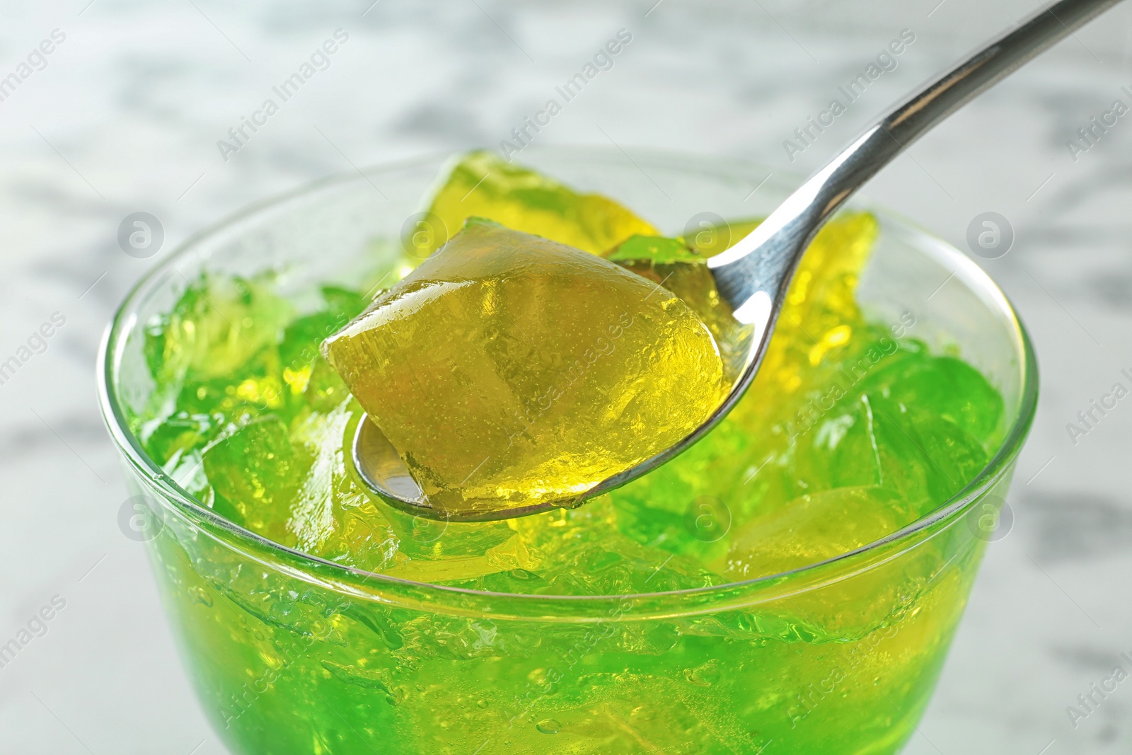 Photo of Spoon with fruit jelly over glass on light background, closeup