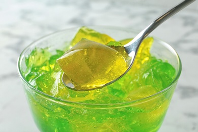 Photo of Spoon with fruit jelly over glass on light background, closeup