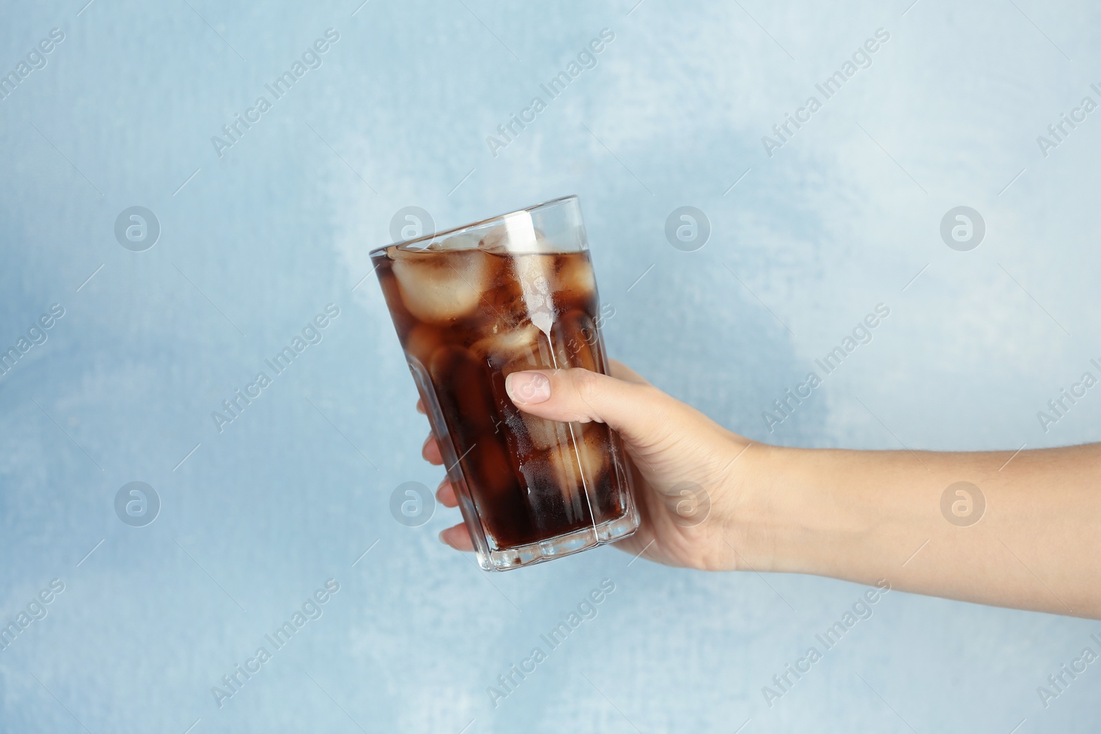 Photo of Woman holding glass of tasty refreshing cola with ice cubes on color background, closeup view