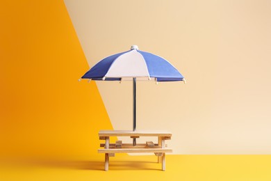 Small wooden holder with toy umbrella on color background