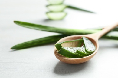 Photo of Wooden spoon with slices of aloe vera on light table. Space for text