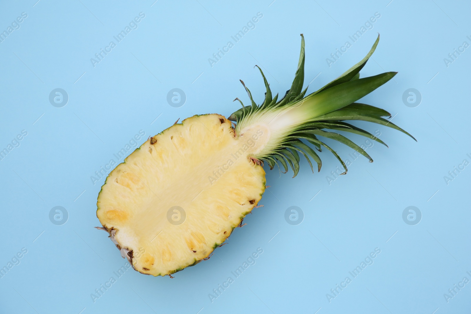 Photo of Half of ripe pineapple on light blue background, top view