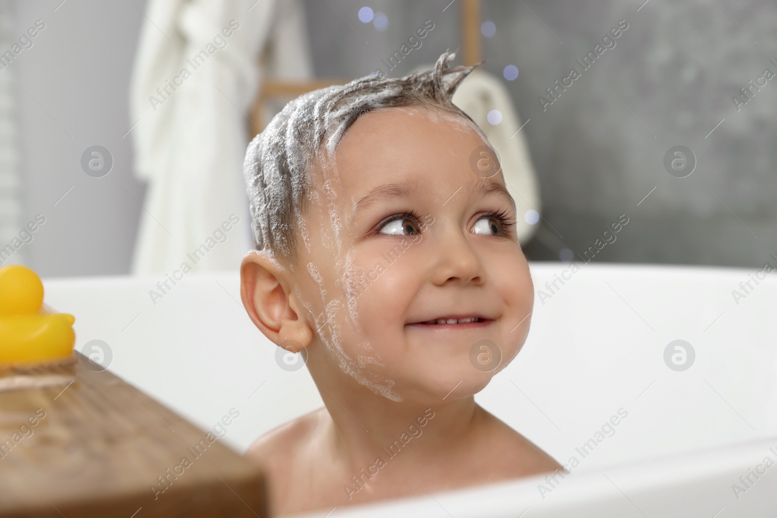 Photo of Cute little boy washing hair with shampoo in bathroom