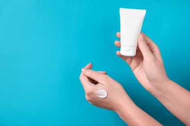 Photo of Woman with tube of hand cream on light blue background, closeup. Space for text