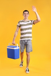 Photo of Man with blue cool box walking and greeting someone on orange background